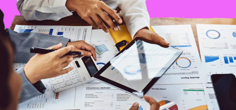 Two people exchanging notes on an ipad surrounded by charts and graphs.