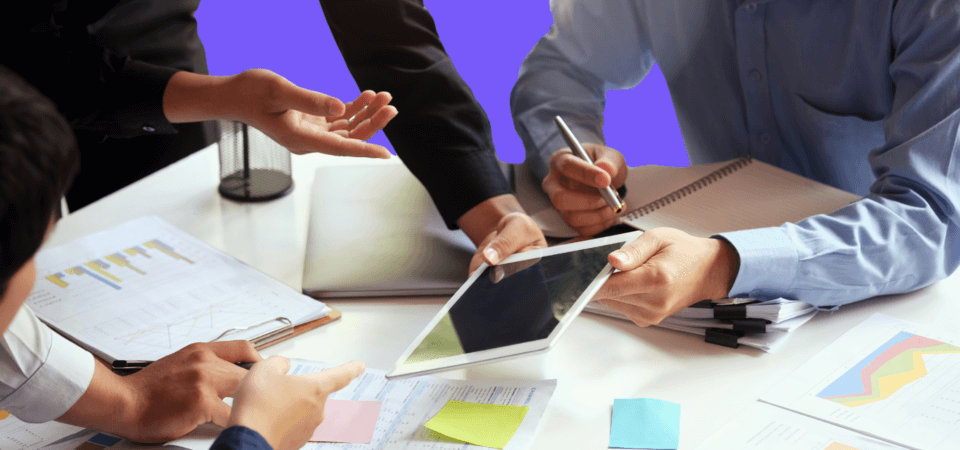 a group of people around a table with scattered papers and an ipad.