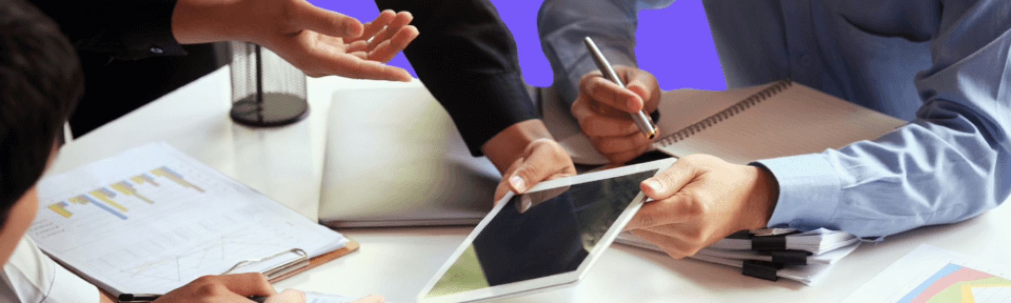 a group of people around a table with scattered papers and an ipad.